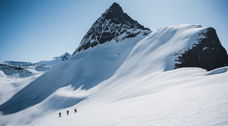 Group of skiers ascending a snowy mountain slope beneath a sharp peak in Sunnmøre, Norway.