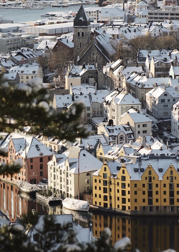 A winter view over Ålesund with snow-dusted rooftops and colourful Art Nouveau houses by the canal.