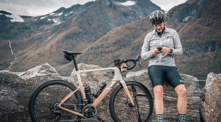 Mountain biker pausing on rocky terrain with scenic peaks in the background.