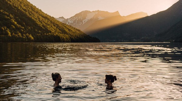 Two swimmers floating peacefully in a fjord at sunset