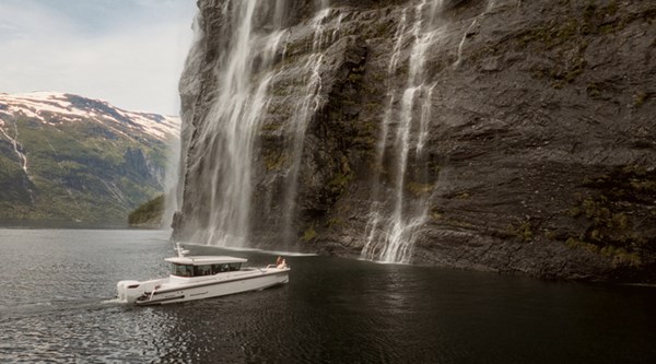 Yacht anchored beneath a tall waterfall cascading down fjord cliffs